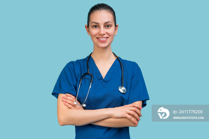 Studio portrait of a young brunette doctor woman in surgical uniform posing over light blue background