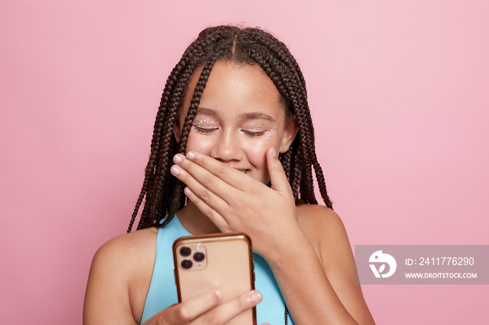 Studio shot of smiling girl with braids looking at smart phone