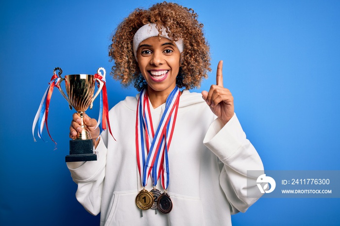 Young african american sporty woman doing sport winning medals and trophy surprised with an idea or question pointing finger with happy face, number one