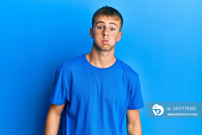 Young caucasian man wearing casual blue t shirt puffing cheeks with funny face. mouth inflated with air, crazy expression.