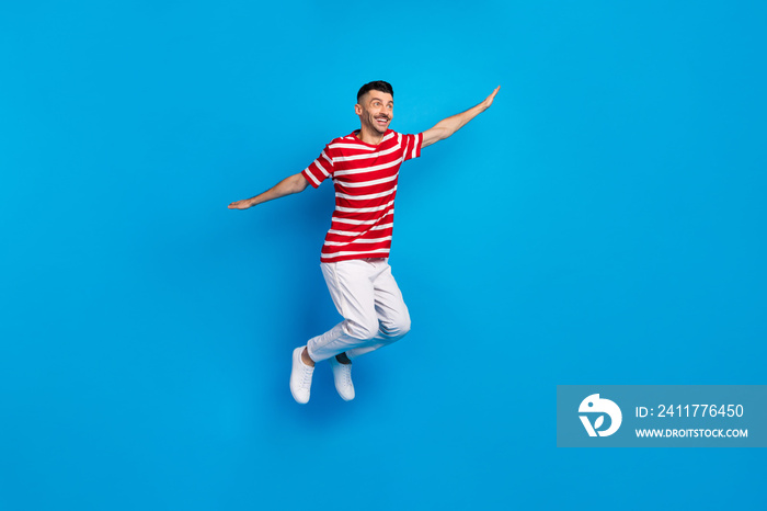 Photo of dreamy sweet young man wear striped t-shirt jumping looking empty space isolated blue color background