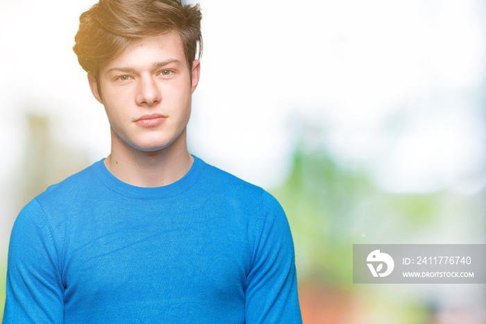 Young handsome man wearing blue sweater over isolated background with serious expression on face. Simple and natural looking at the camera.