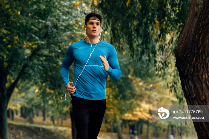 Horizontal image of young jogger man jogging outdoor in the nature background. Fitness male exercising in the park, wearing blue and black sportswear. People and sport concept