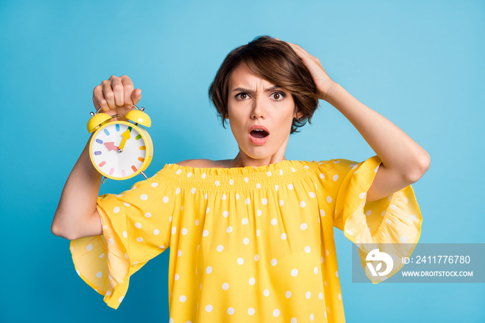 Photo portrait of upset woman holding alarm clock isolated on vivid blue colored background