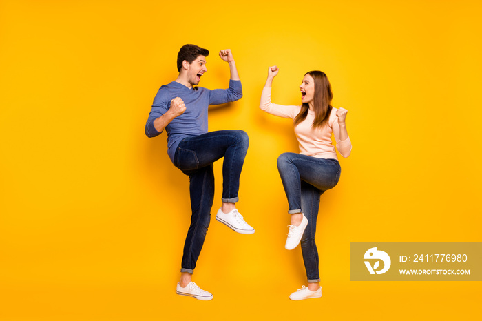 Full body photo of delighted emotional couple celebrate victory raise fists scream yeah wear denim jeans sneakers isolated over yellow color background