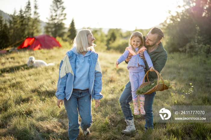 Young caucasian couple with little girl have fun while travel in the mountains. Happy family spending summer vacation at campsite. Father tossing daughter in his arms