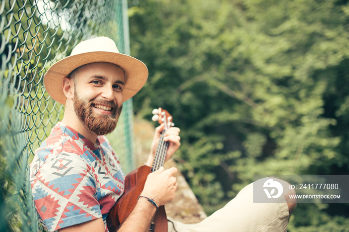 Man with beard and hat playing ukulele in nature