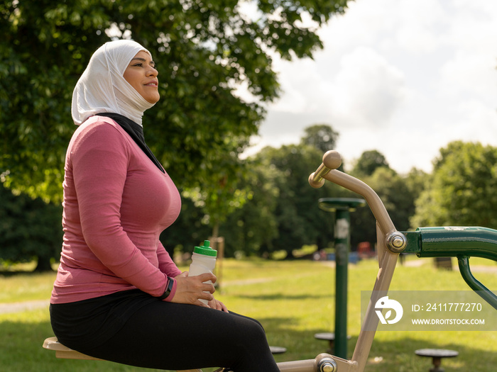 UK,Sutton,Smiling woman in headscarf resting at park gym