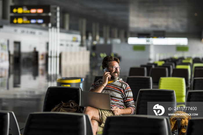 Adult man travel at the airport sit down at the gate waiting for his airplan flight - delay conncept and people working everywhere with laptop computer technology - caucasian male traveling