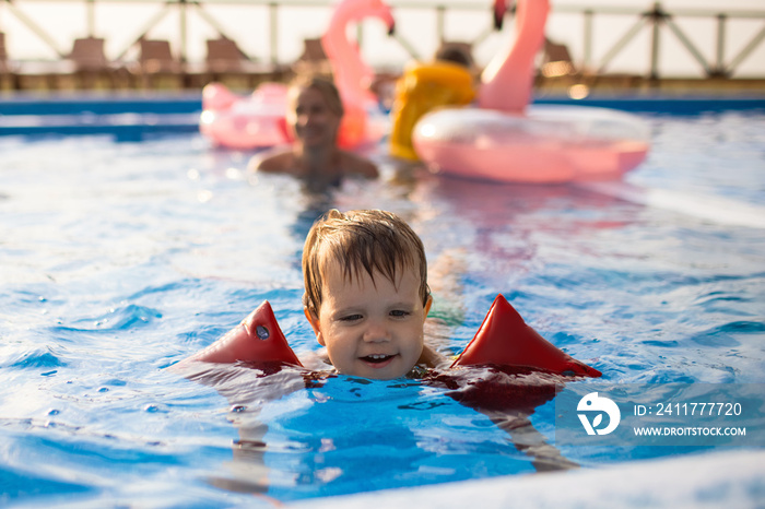 A boy with armbands and a disgruntled face, trying to get out of a pool of clean water and calling for his mother