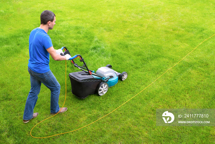 Gardener in the garden mows grass with a lawn mower. Side view