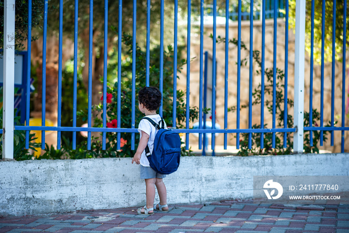 Kid with school backpack look on schoolyard towards beautiful garden. Schools and preschools remain locked for children during lockdown, coronavirus pandemic and second wave of covid-19. Soft focus.