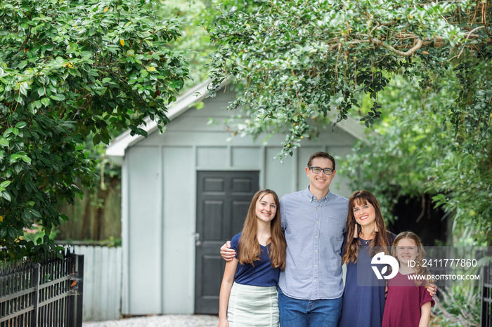 A family of a mother and father and two daughters standing outside in front of a small storage building