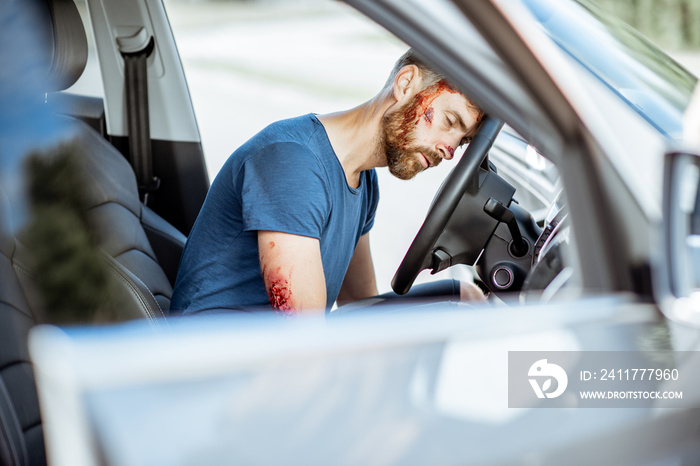 Injured man with a broken head and bleeding wounds sitting on the driver seat without consciousness after the road accident inside the car