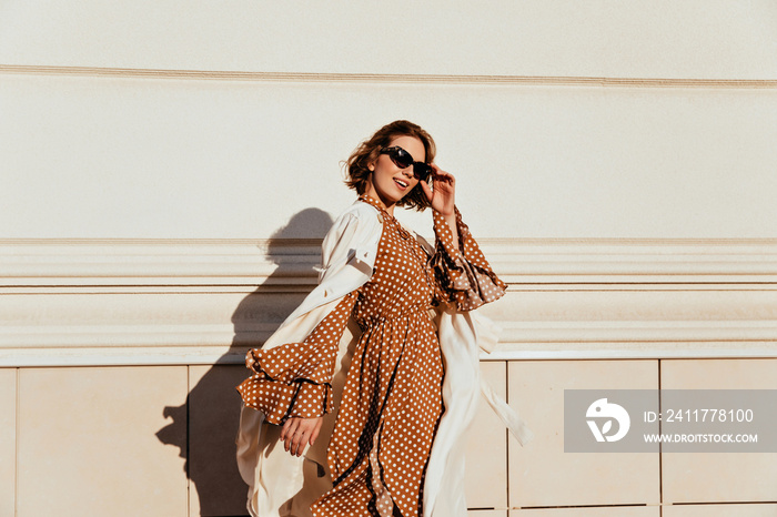 Pretty woman in long brown dress enjoying sunny day. Lovable white girl in retro attire walking down the street.