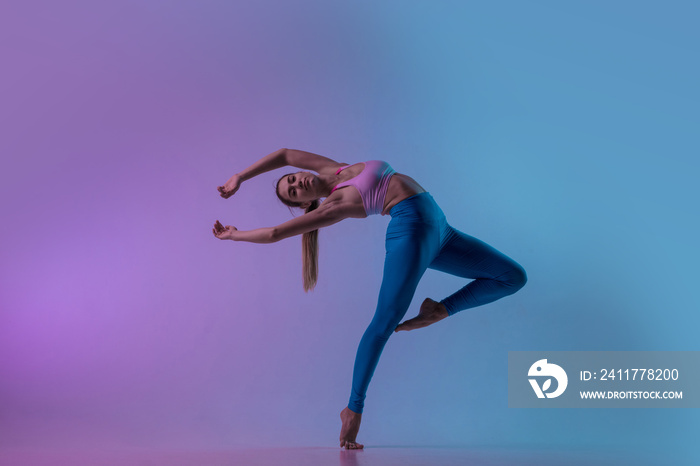 Graceful. Young sportive woman training isolated on gradient studio background in neon light. athletic and graceful. Modern sport, action, motion, youth concept. Beautiful caucasian woman practicing.