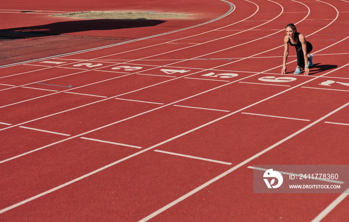 Young runner woman in sportwear getting ready to run sprint at low start on stadium track with red coated at bright sunny day