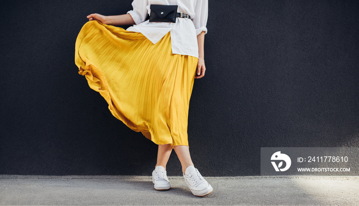 Cropped body shot of attractive woman in beautiful yellow skirt. Caucasian female fashion model standing over gray wall background outdoor with copy space.