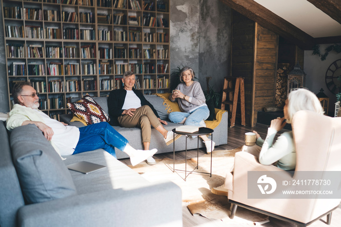 Group of elderly friends sitting in living room chatting having hot drinks