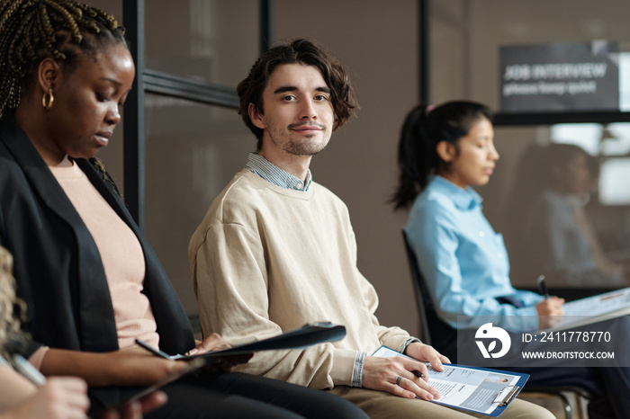 Portrait of young candidate sitting in waiting room with resume and looking at camera