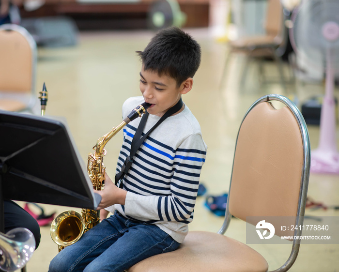 Little asian musician boy playing saxophone instrument