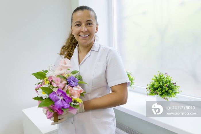 Woman nurse with bouquet of flowers, smiling near the window in the hospital. National Doctor’s day