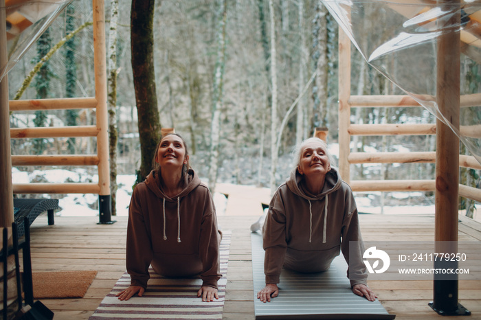 Woman senior and young relaxing at glamping camping tent. Women family elderly mother and young daughter doing yoga and meditation indoor. Modern zen-like vacation lifestyle concept