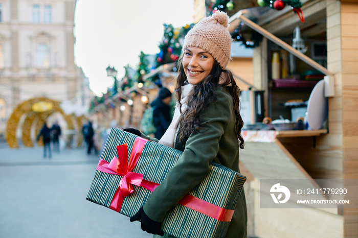 Happy woman with gift box enjoying at Christmas market and looking at camera.