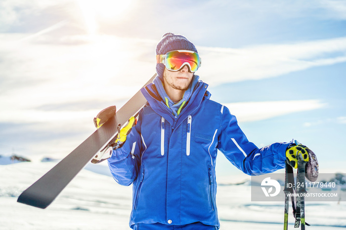 Skier ready holding skiing equipment with sun back light on ski slope