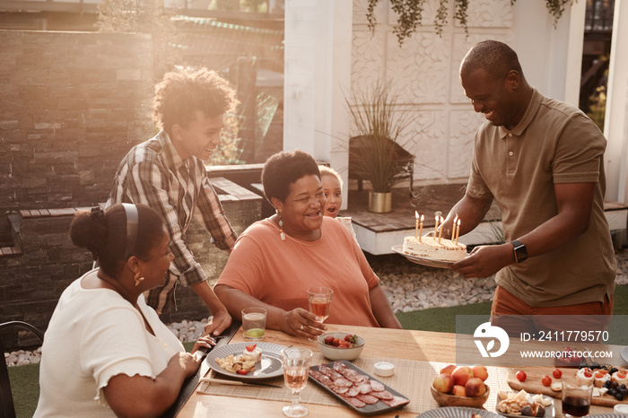 Portrait of happy African-American family celebrating grandmothers Birthday outdoors lit by sunlight, copy space