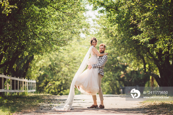 Happy bridegroom raises bride in summer park. man raised and hug woman to her arms. Newly wedded couple in the park. Just married. Walk in the park and hug. Newlyweds having fun. rustic wedding