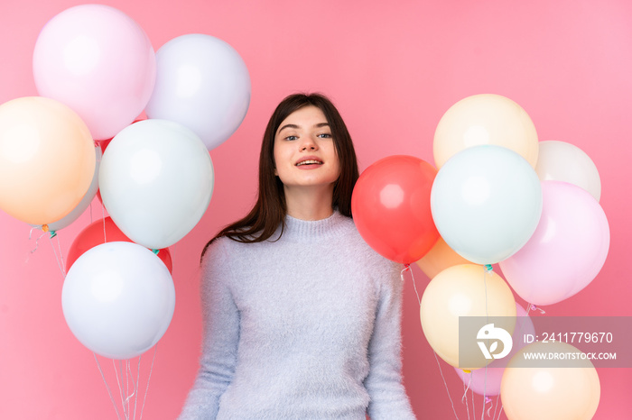 Young Ukrainian teenager girl holding lots of balloons over isolated pink background