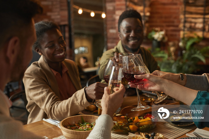 Portrait of happy African-American couple clinking glasses while enjoying dinner party with friends and family in cozy interior