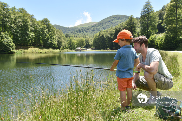 Father and son fishing together by mountain lake