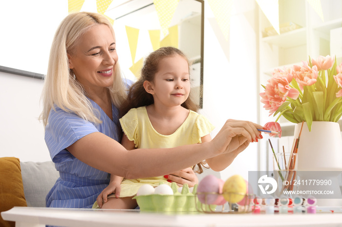 Little girl and her grandmother painting Easter eggs at home