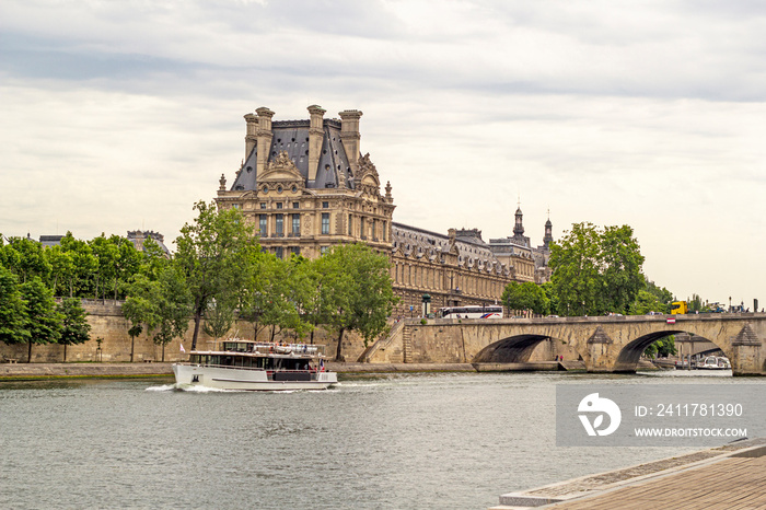 looking across the river seine at the corner of the lourve palace art museum in paris france with a tourist boat crusing up the river. on a warm but cloudy summer afternoon