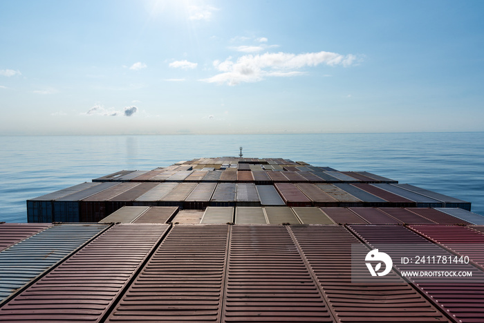 Fully loaded container ship sailing through a blue, calm ocean. View on the top of the containers loaded on deck of the cargo ship.