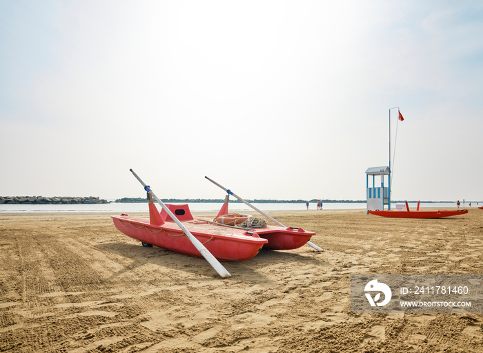 Lifeguard tower next to a lifeboat on the beach on a sunny summer morning, in the background some bathers cooling off on the Adriatic coast, Italy.