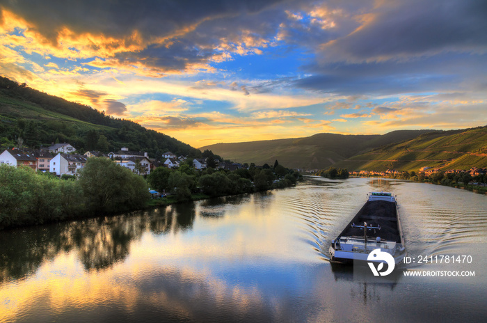 Beautiful vibrant sunset view of the river Moselle at the small wine growing town Zell (an der Mosel) with hills full of grape vines with a barge on the river