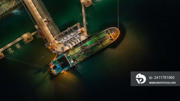 Aerial top view oil tanker ship at terminal industrial port at night for transfer crude oil to oil refinery, Business import export oil and gas petrochemical.