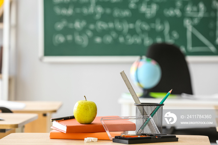 Apple with books, pen cup and school stationery on table in classroom