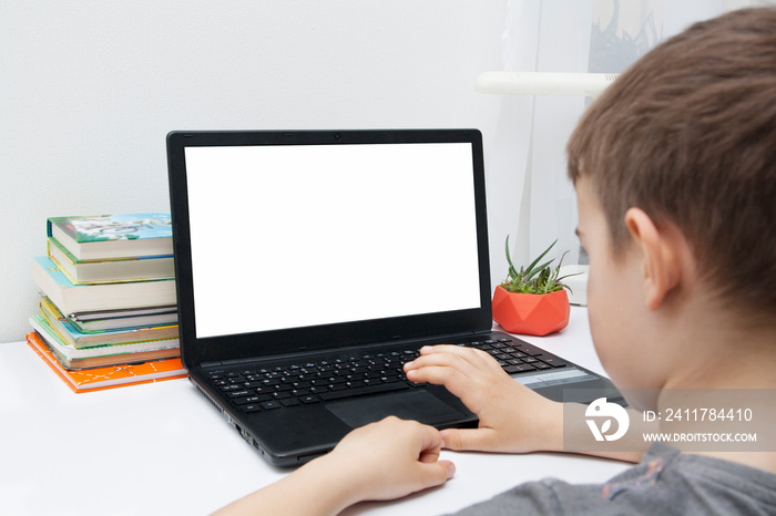 A boy sits at a desk with a laptop. Online Home Learning Concept. Mock up laptop PSD.