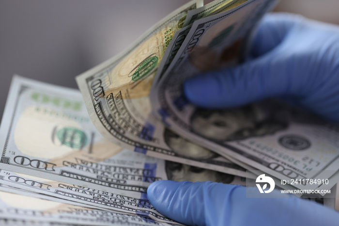 Hands in blue gloves hold one hundred dollar bills. How to disinfect money from coronavirus concept