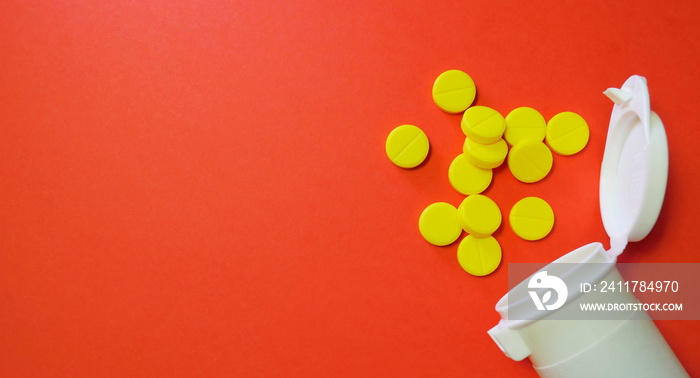 Yellow pills and white bottle with copy space on red background