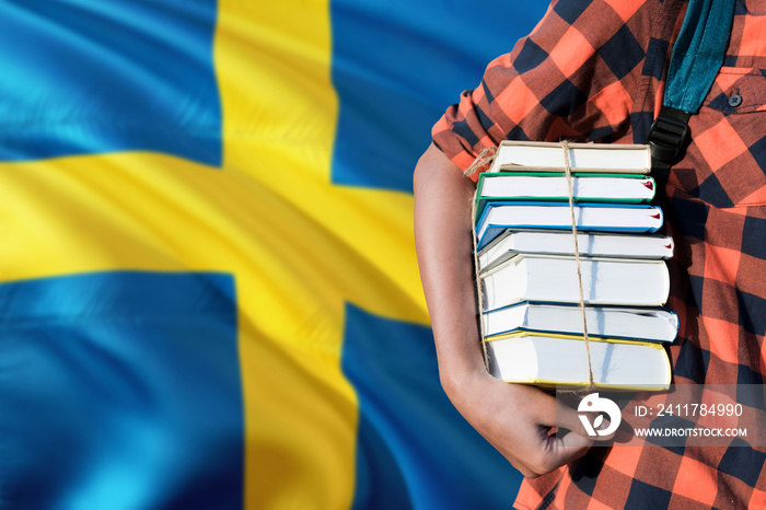 Sweden national education concept. Close up of teenage student holding books under his arm with country flag background.