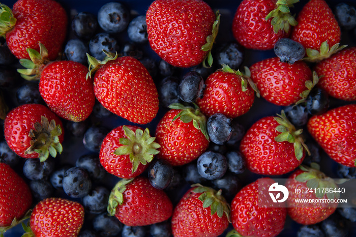 Background of assorted fresh berries of red juicy strawberries and blue blueberries close-up.