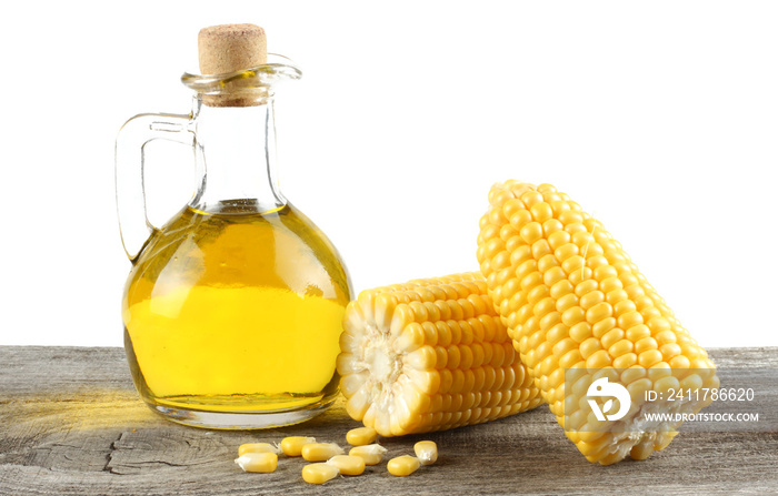 corn oil in glass jug with corn on cob on old wooden table with white background