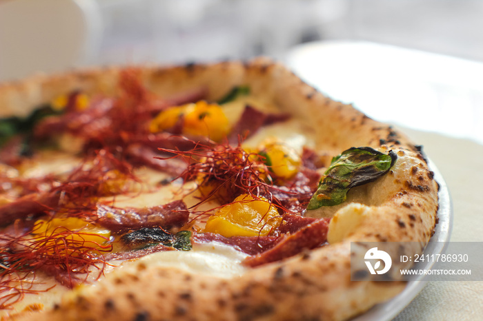 close detail of Spicy gourmet pizza with yellow Piennolo tomatoes, Caserta salami, chilli pepper strands, Agerola provola and parmesan cheese in an Italian pizzeria