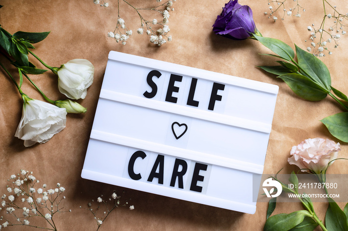 Self-care word on lightbox and flowers on color background flat lay. Take care of yourself