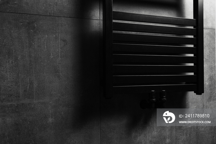 Photo of black matte heated towel rack, in the bathroom with dark grey walls.